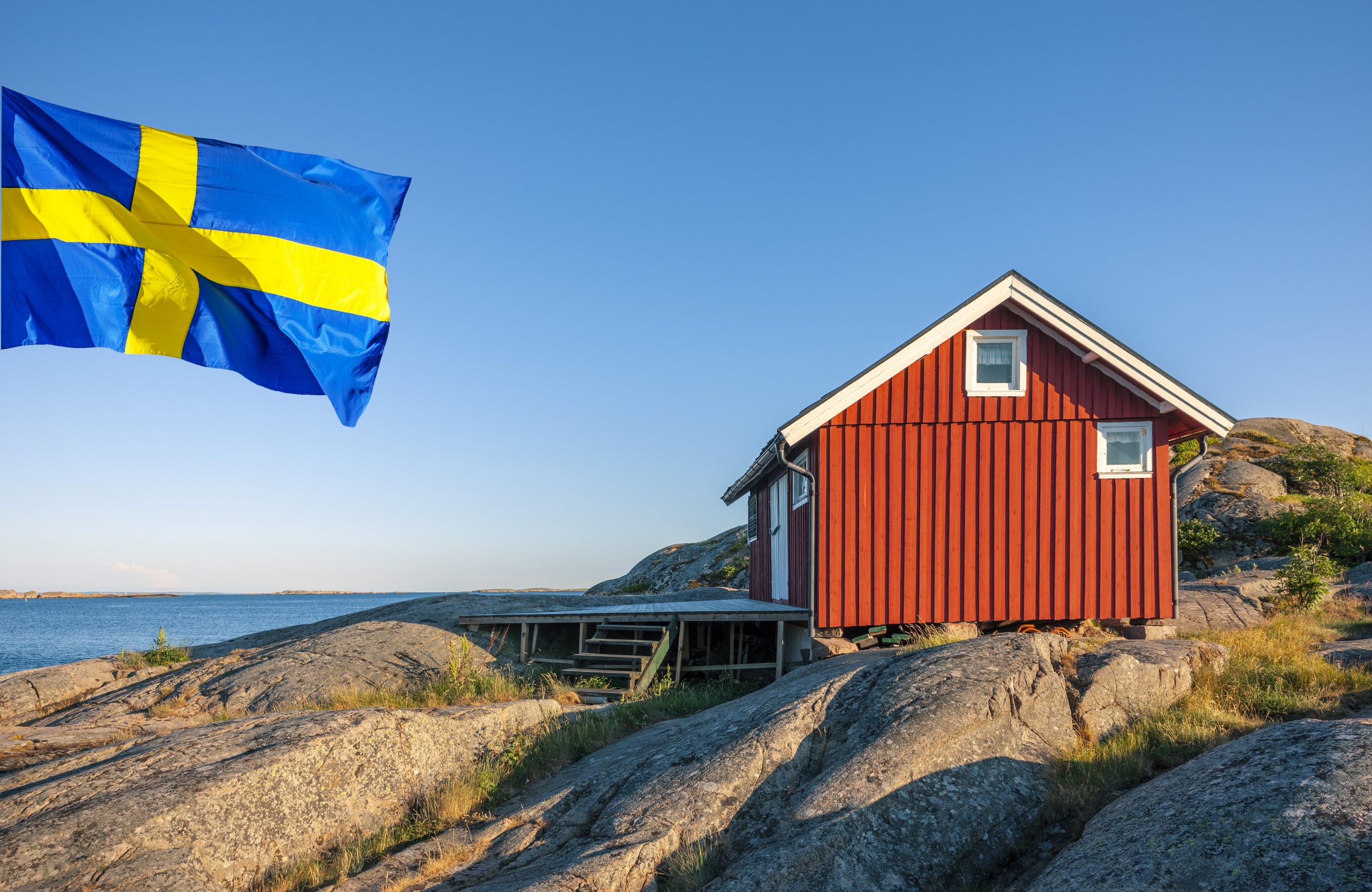 Hytte på store sten ud til vandet med et svensk flag flagrende ved siden af